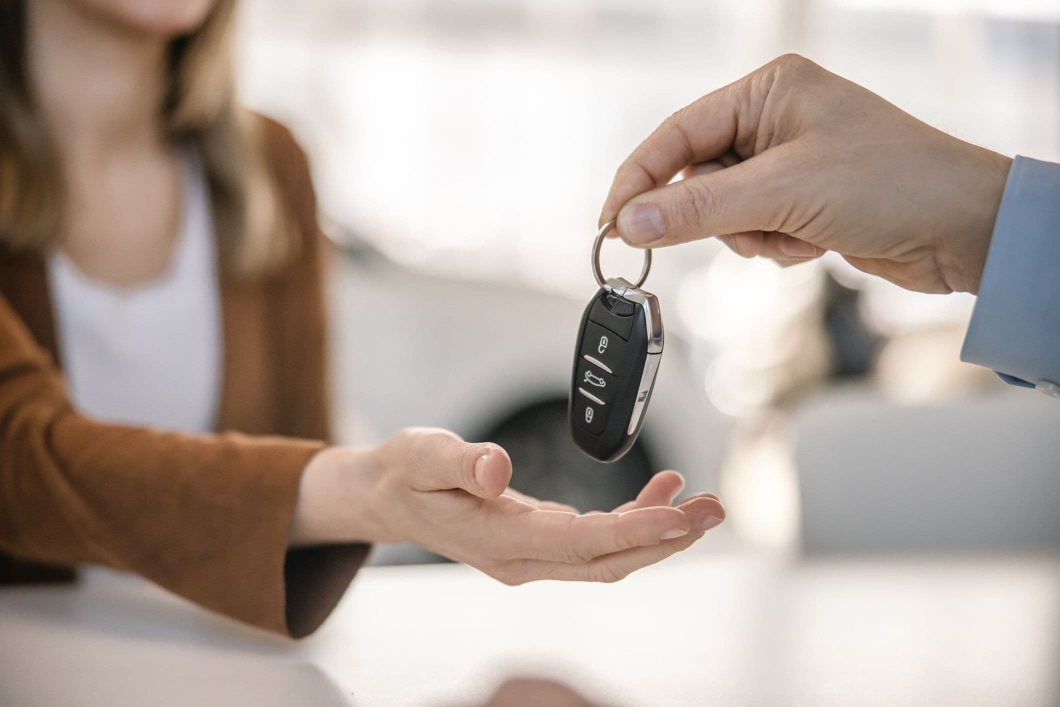 Üks käsi annab autovõtmed teisele käele, taustal hägune siseruum