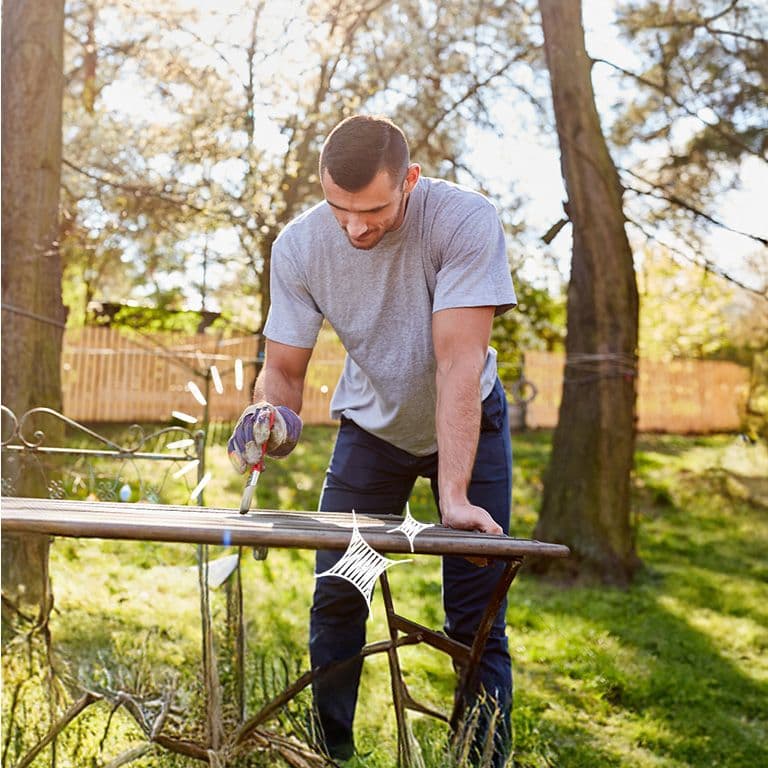 Inimene udustatud näoga hoiab nutitelefoni, istudes laua taga, millel on kollaste lillede vaas; taustal on köögikapid