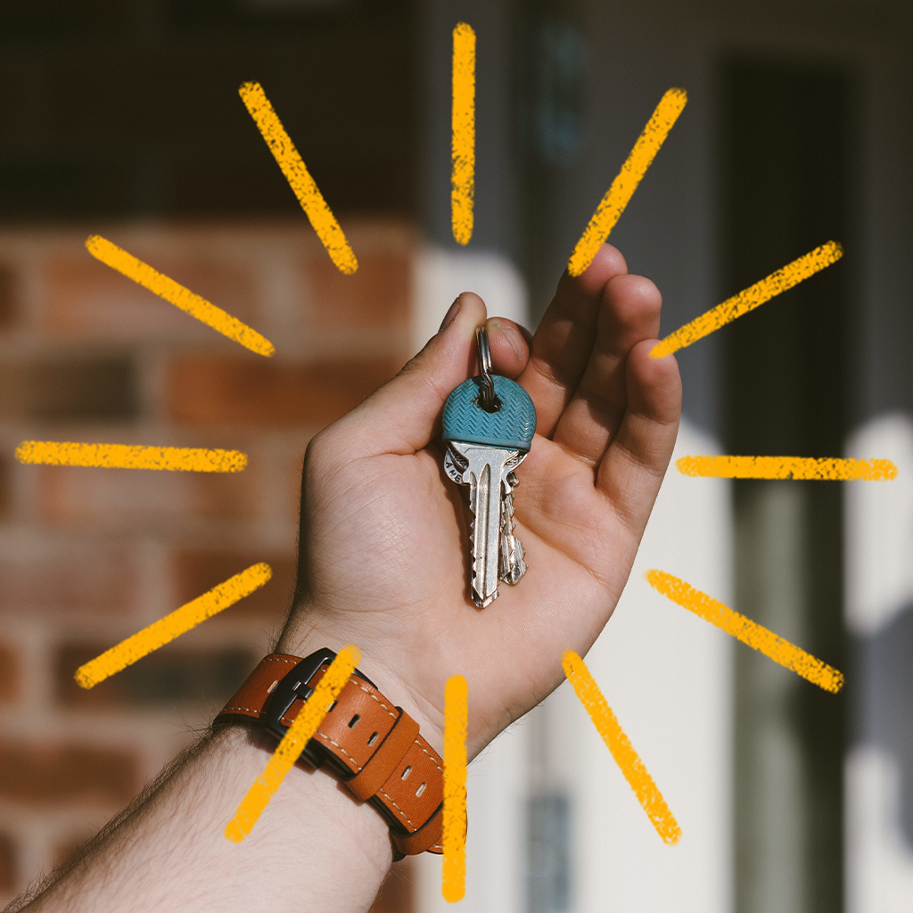 Käsi hoiab sinise peaga võtit, taustal tellissein ja ukseraam