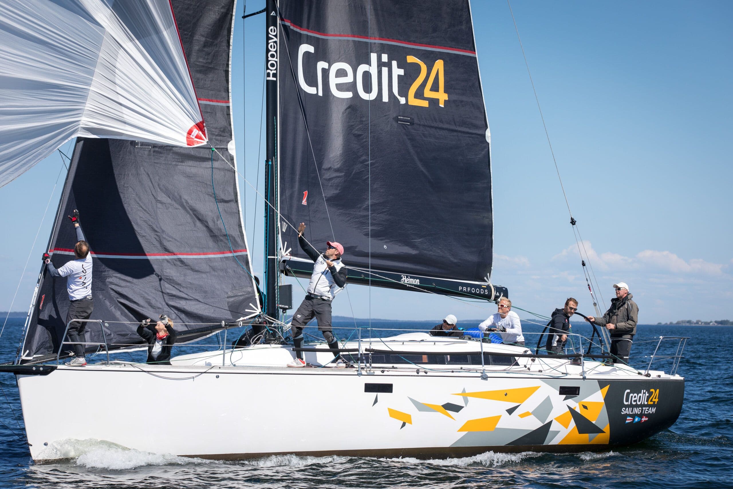 Purjekas "Credit24" meeskonnaga sõidab vee peal, taustal selge taevas.